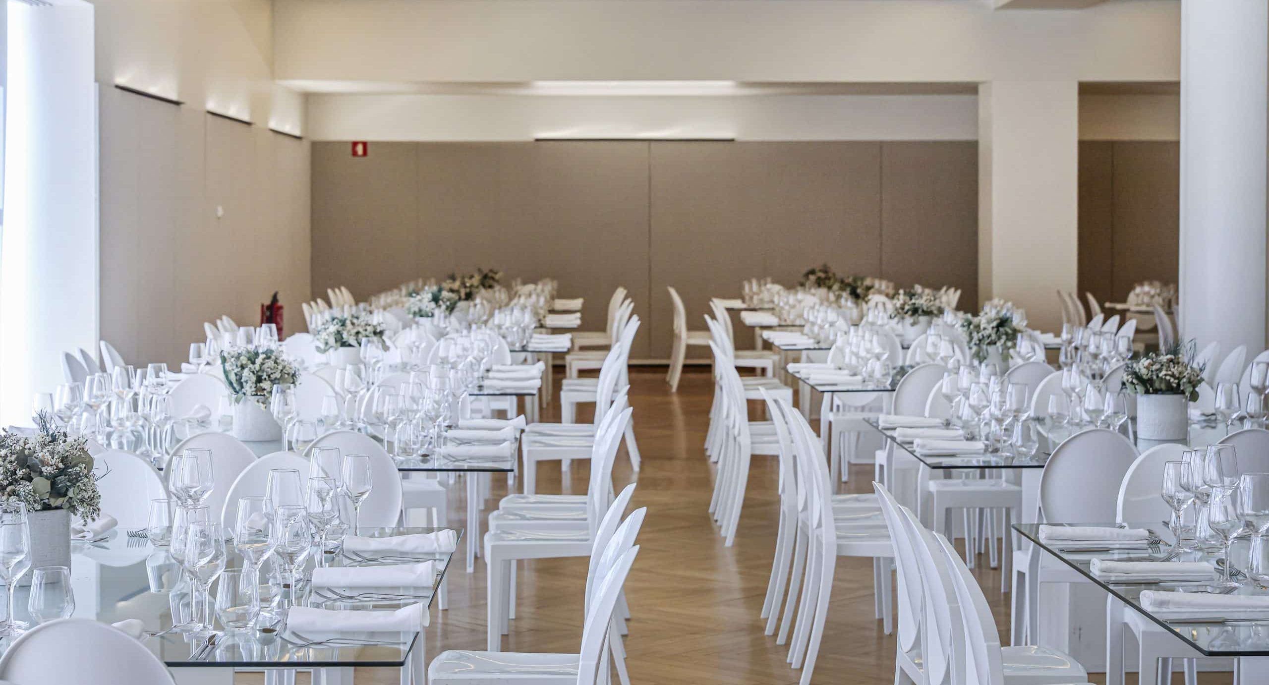 http://Sala%20Vitorino%20Nemésio%20decorada%20para%20serviço%20de%20catering,%20com%20mesas%20brancas,%20flores%20e%20vidro,%20ideal%20para%20comemorações%20elegantes.
