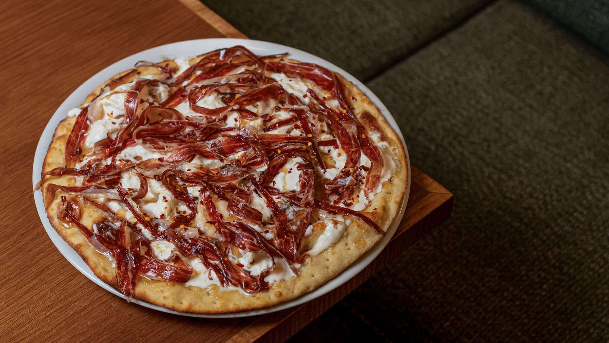 http://Pizza%20com%20molho%20de%20tomate,%20queijo%20e%20fatias%20de%20presunto%20sobre%20uma%20superfície%20de%20madeira,%20pronta%20para%20ser%20servida.%20Um%20dos%20pratos%20servidos%20pelo%20Resaturante%20Esteoeste.